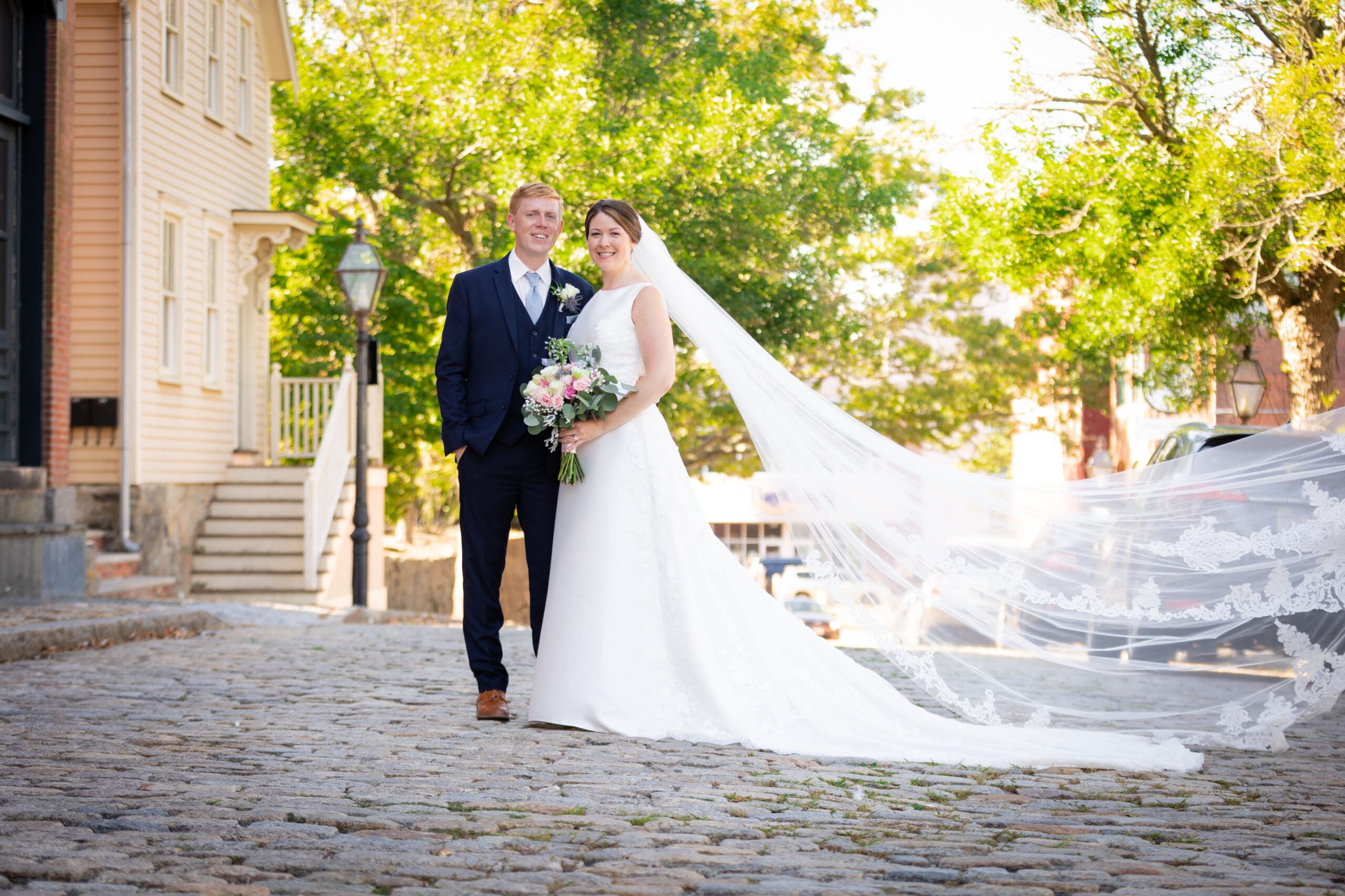 Erin and Alex's wedding portrait, Erin's long veil blowing flowing on the historic cobblestone streets of New Bedford, Massachusetts